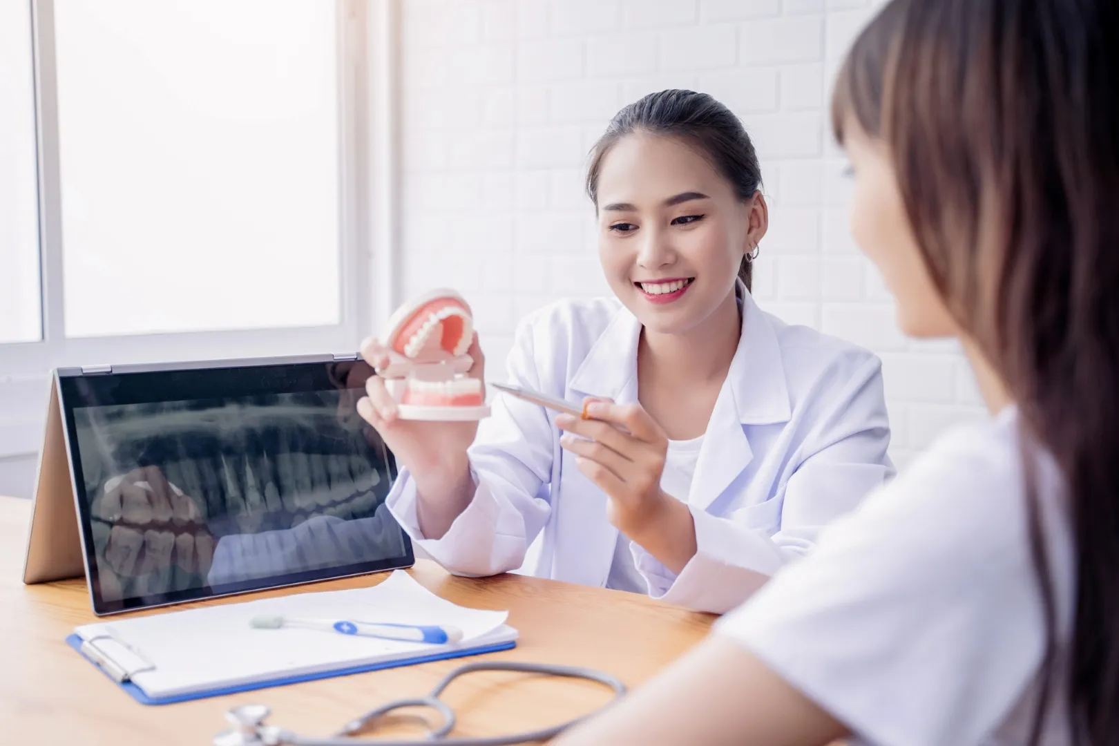 Dentist smiling while showing a dental model and X-ray on a tablet to a patient.