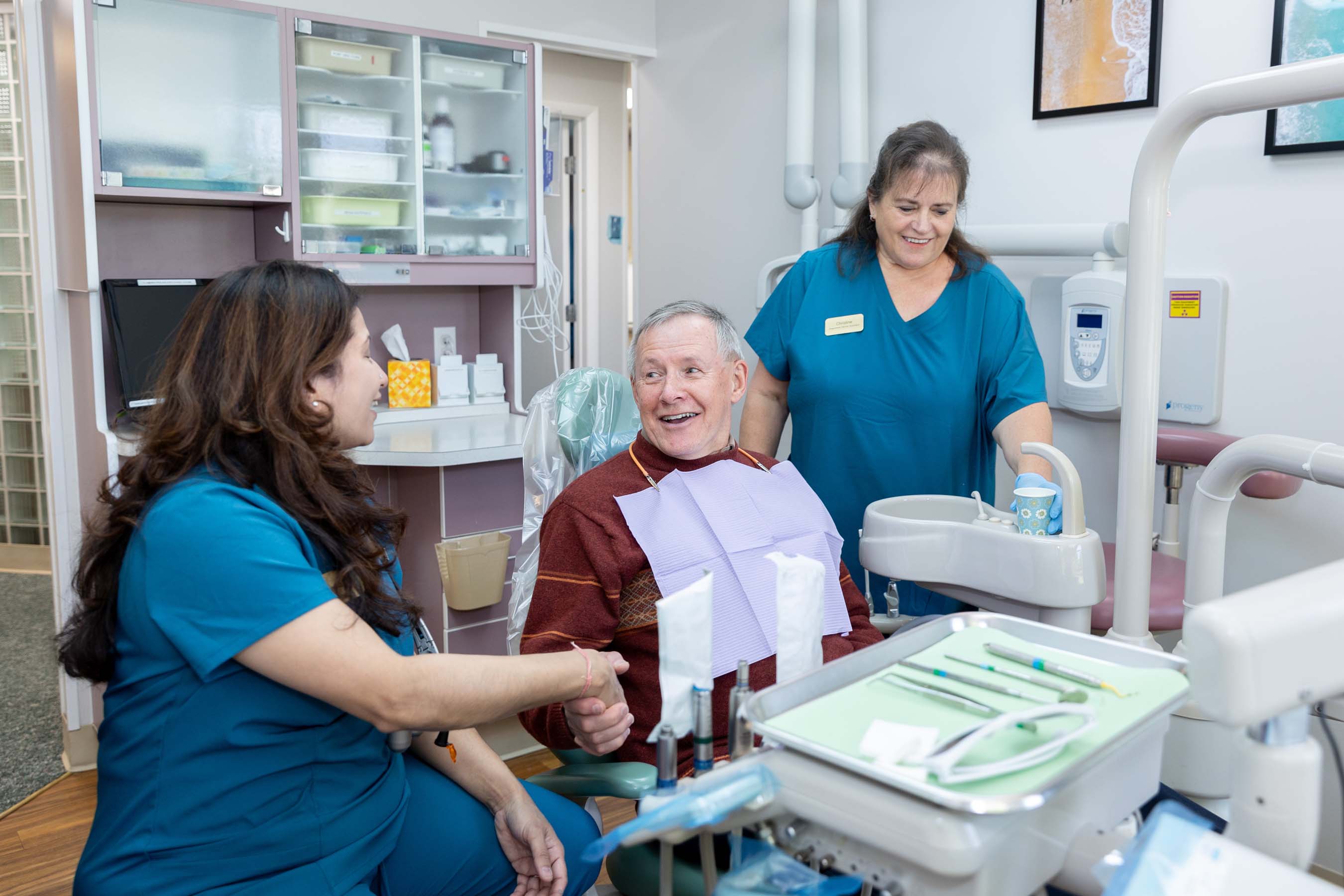Dental patient smiling and shaking hands with female dentist while dental assistant watches in the office.